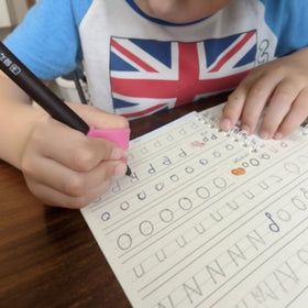 Review / Child writing on a magic copybook with a pen, wearing a shirt with a UK flag .