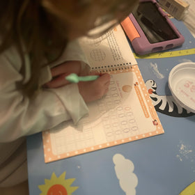 Child writing on a worksheet with a green pen at a desk.
5-star verified review - 5-year-old girl learning to write numbers using TinkerMindz magic practice copybooks