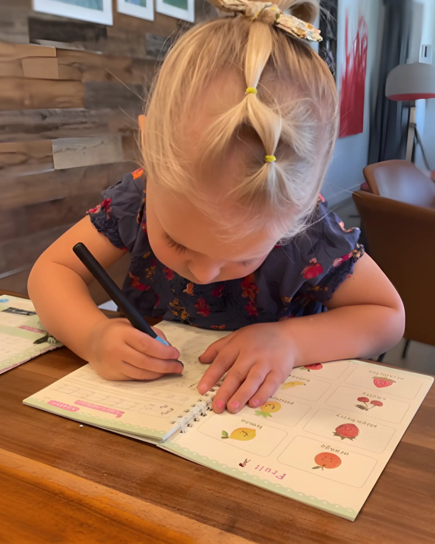 Young girl writing in a notebook with a pen at a wooden table.